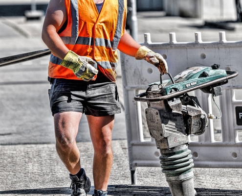 Baustellenfotografie eines Arbeiters mit Rüttelstampfer zur Verdichtung des Untergrundes für Straßenbauarbeiten in Braunschweig.